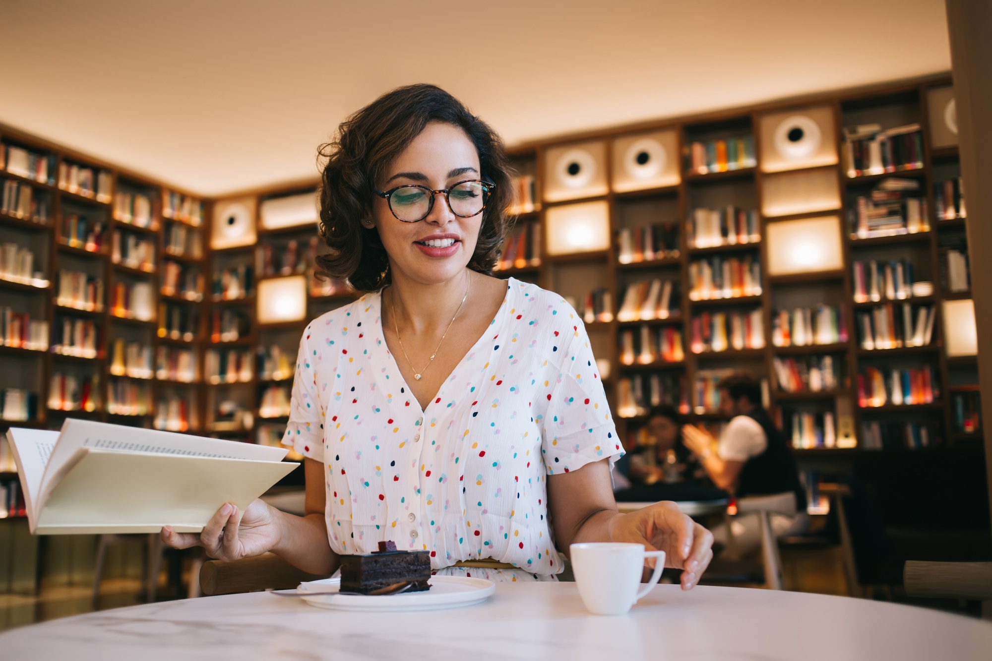 Smiling woman with textbook and hot drink in cafeteria